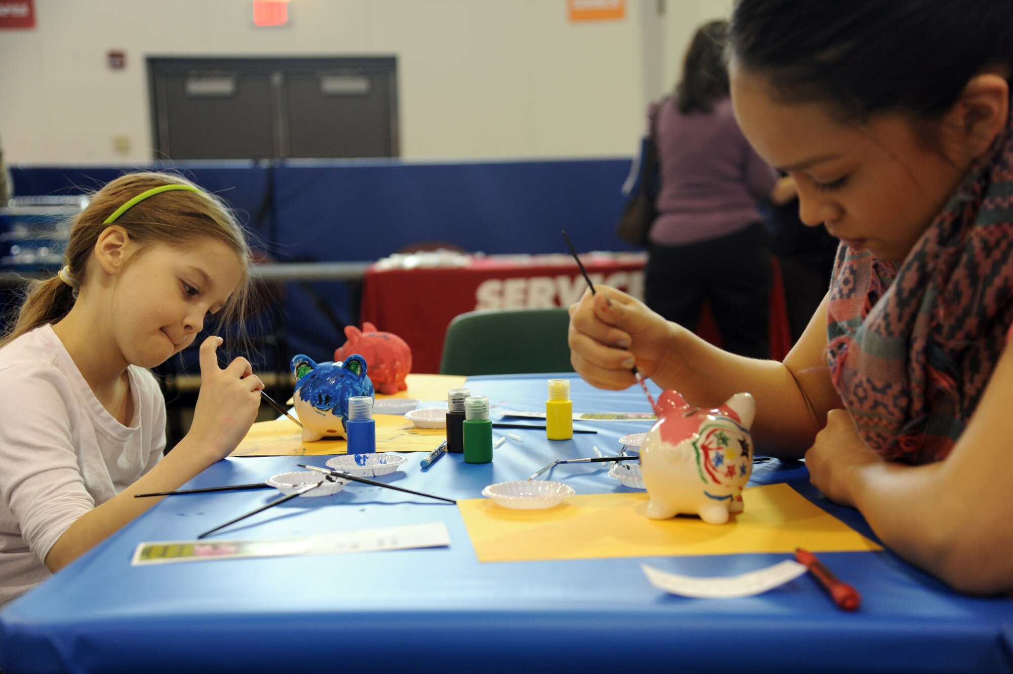 Daria McNerney, 8, and Nelenah Greyeyes, 15, paint piggy banks at the Military Saves Financial Fair on Grand Forks Air Force Base, N.D., Feb. 25, 2015. The fair was hosted by the Airman & Family Readiness Center and featured activities for children and helpful finance information for adults. (U.S. Air Force photo by Tech. Sgt. David Dobrydney/released)
