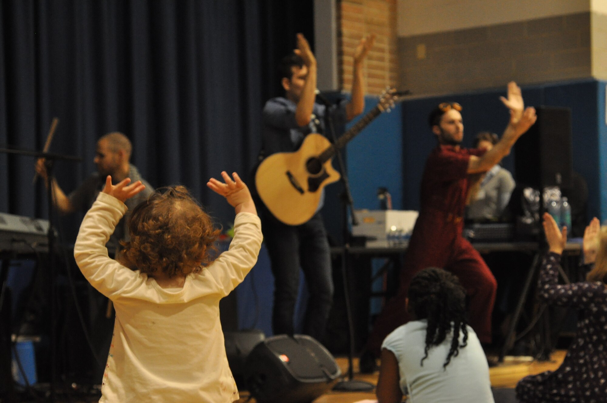 A toddler raises her hands as the group claps to the beat of band member, Alex “Jumpsuit” MacDonald of the Tim and the Space Cadets, tap dances at the Prairies Youth Center at Wright-Patterson AFB. (U.S. Air Force photo/Myra Saxon)