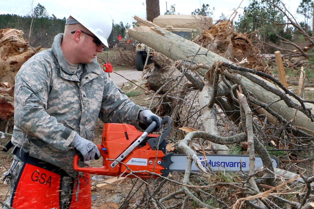 A soldier saws through tree branches to open a blocked road in Essex County, Va., Feb. 25, 2016. Virginia National Guard photo by Alfred Puryear