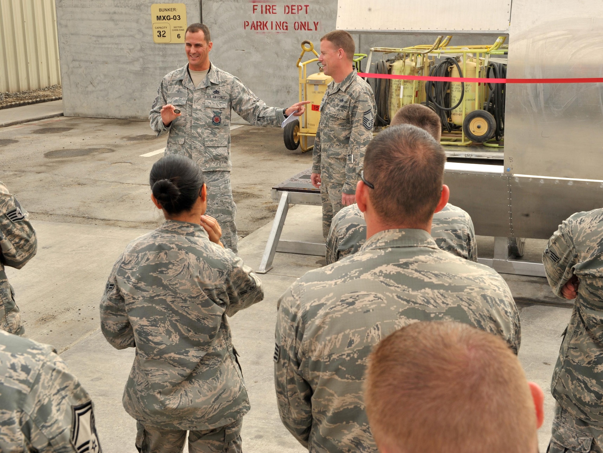 Chief Master Sgt. Robert, 380th Expeditionary Civil Engineer Squadron Fire Department fire chief, presents the unit’s coin to Fabrication Flight Airmen at the unveiling of the fire department search and rescue aircraft trainer at an undisclosed location in Southwest Asia, Feb 19. Completion of the trainer means firefighters here can now practice cutting into the frame of an aircraft, an experience previously only known to be offered during their technical school at Goodfellow Air Force Base, TX. and in real life emergencies. (U.S. Air Force photo by Staff Sgt. Kentavist P. Brackin/released)