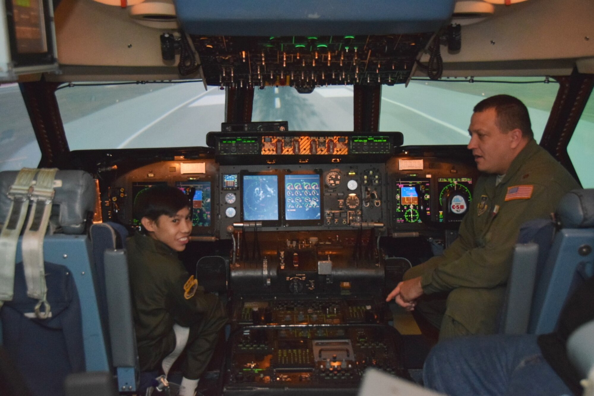 Zach Gutierrez, the 433rd Airlift Wing’s Pilot for a Day, talks with Maj. Chris Melton, a C-5A Galaxy pilot and 68th Aerial Squadron Director of Operations. Zach, accompanied by television media and his parents, was able to try his hand at flying the C-5 simulator around Honolulu.  (U.S. Air Force photo by Tech. Sgt. Carlos J. Trevino)
