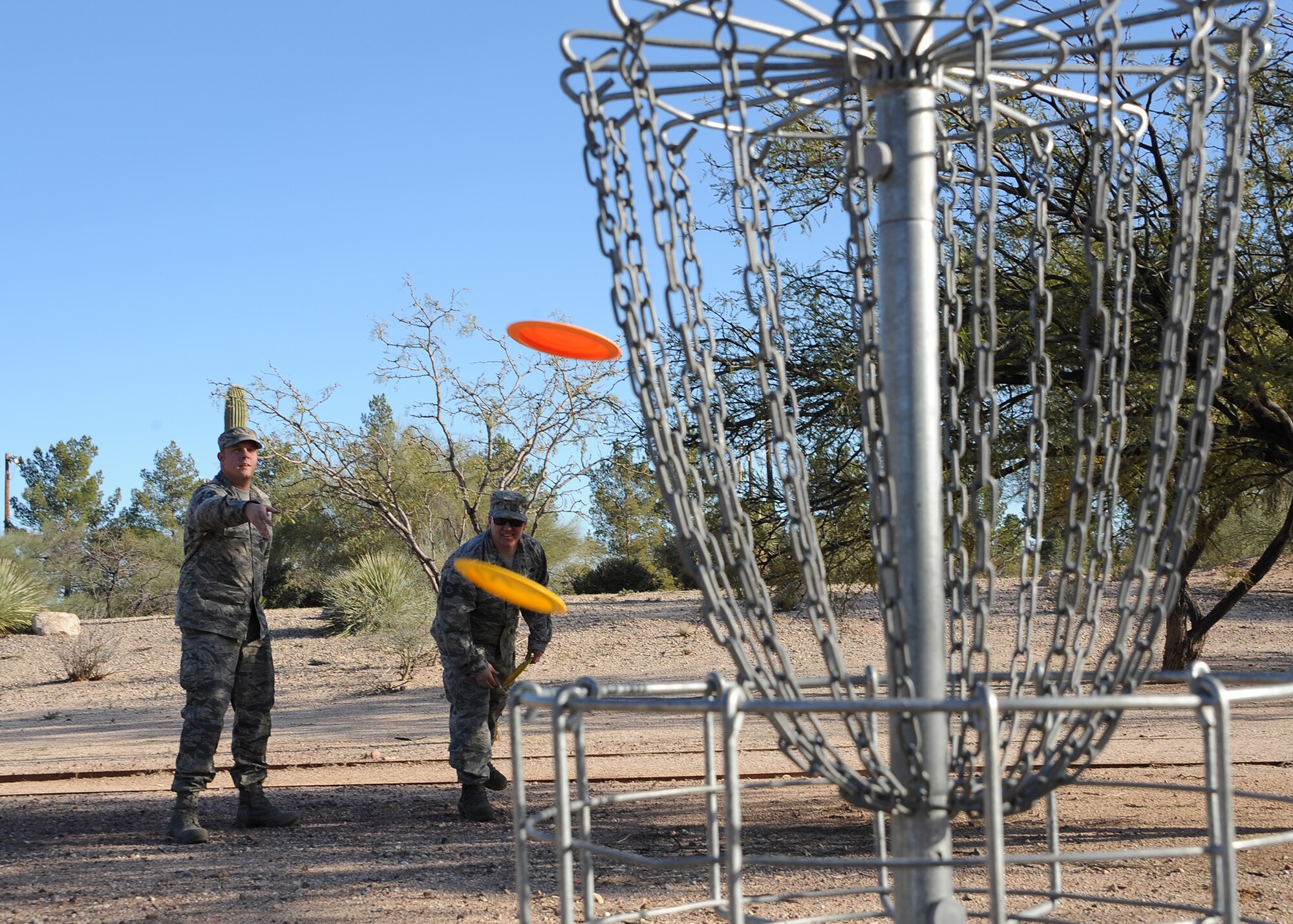 U.S. Air Force Tech. Sgt. Timothy Doub, 355th Electronic Maintenance Squadron C-130 isochronal maintenance lead technician, and Tech. Sgt. Donald Brown, 355th Electronic Maintenance Squadron C-130 dock coordinator, toss discs into the disc golf target basket near the future disc golf course site at Davis-Monthan Air Force Base, Ariz., Feb. 10, 2016. The two designed a course and presented their idea at the InnovateDLT event, which gave Airmen a direct line to the base commander and allowed them to propose an improvement that will impact members of the base. (U.S. Air Force photo by Airmen 1st Class Ashley N. Steffen/Released) 