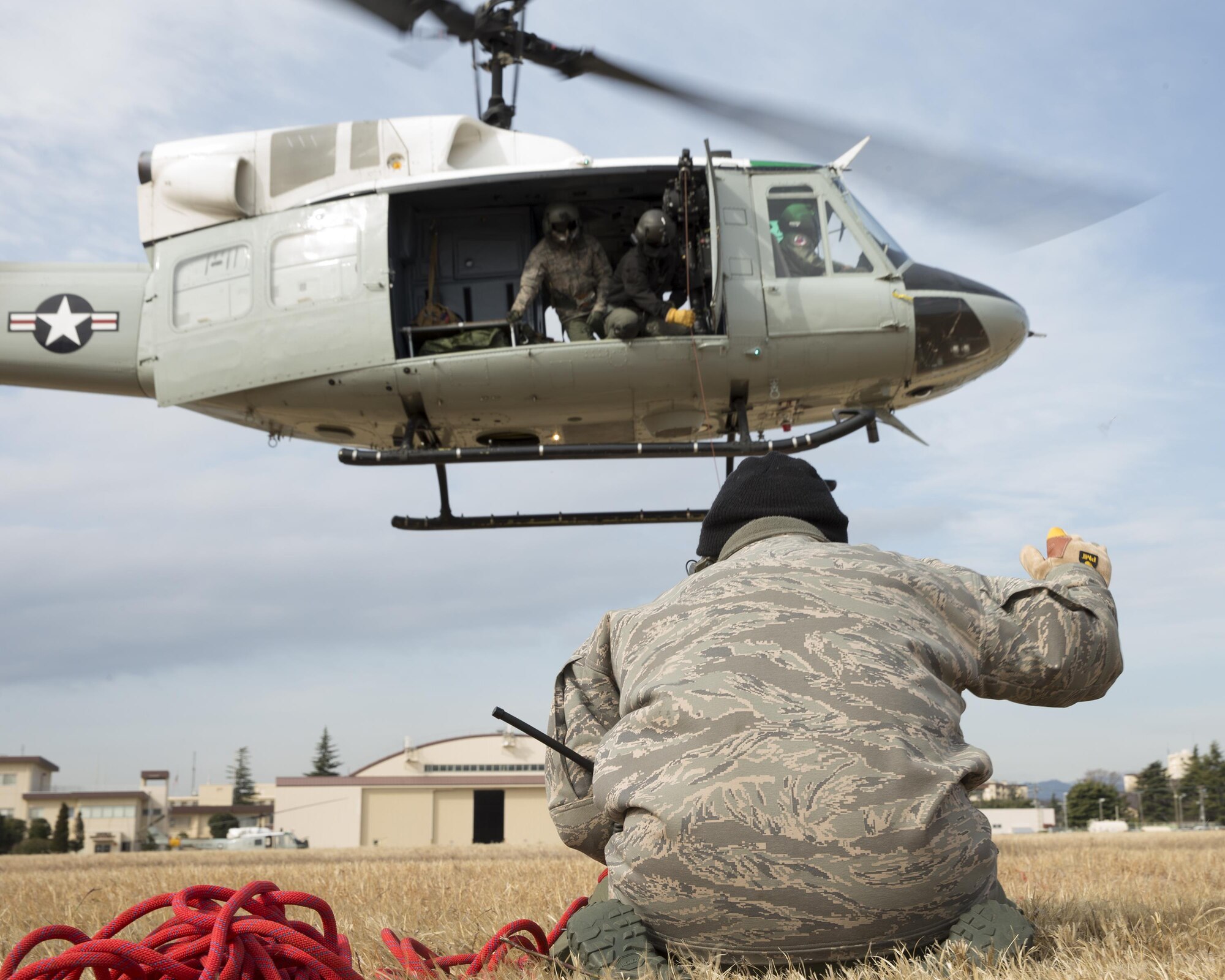 Tech. Sgt. Christopher Rector, 459th Airlift Squadron flight engineer, supervises a UH-1 Huey lifting a testing weight, during hoist training at Yokota Air Base, Japan, Feb. 22, 2016. The 459th AS recently improved their search and rescue capabilities by outfitting two Hueys with new rescue hoists. (U.S. Air Force photo by Osakabe Yasuo/Released)