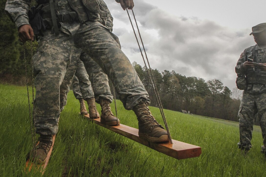 Reserve Officer Training Corps cadets from four Upstate South Carolina colleges work together to walk a specified distance in an allotted time on two wood boards, without their feet slipping off, as part of a team-building challenge during a joint field training exercise in the Clemson Forest hosted by the Clemson University ROTC, March 27, 2015. (U.S. Army photo by Sgt. Ken Scar)