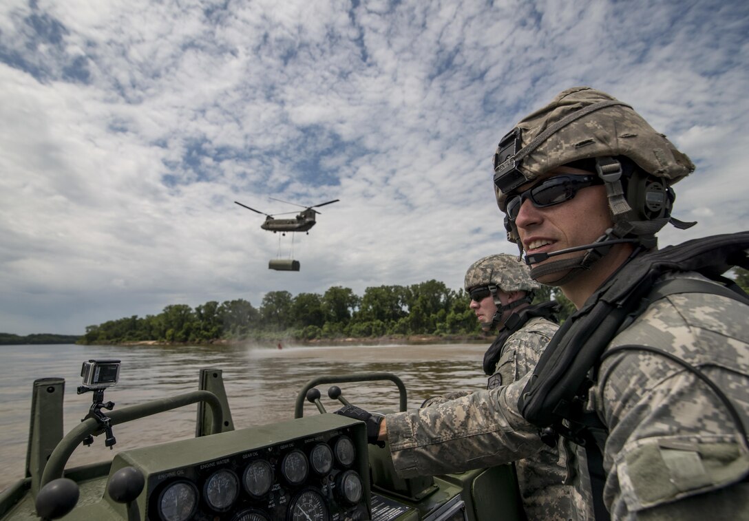 Staff Sgt. Chad Bentley, bridge crew member, and Spc. Ben Adams, medic, both from Tulsa, Okla., with the 341st Engineer Company (Multi-Role Bridge), ride on an MK-2 boat as safeties while a Chinook caries a boat bay to drop it in the Arkansas River, July 31. Soldiers from various Army Reserve and active duty units trained together at River Assault, a bridging training exercise involving Army Engineers and other support elements to create a modular bridge on the water across the Arkansas River at Fort Chaffee, Ark. The entire training exercise lasted from July 28 to Aug. 4, 2015, involving one brigade headquarters, two battalions and 17 other units, to include bridging, sapper, mobility, construction and aviation companies. (U.S. Army photo by Master Sgt. Michel Sauret)