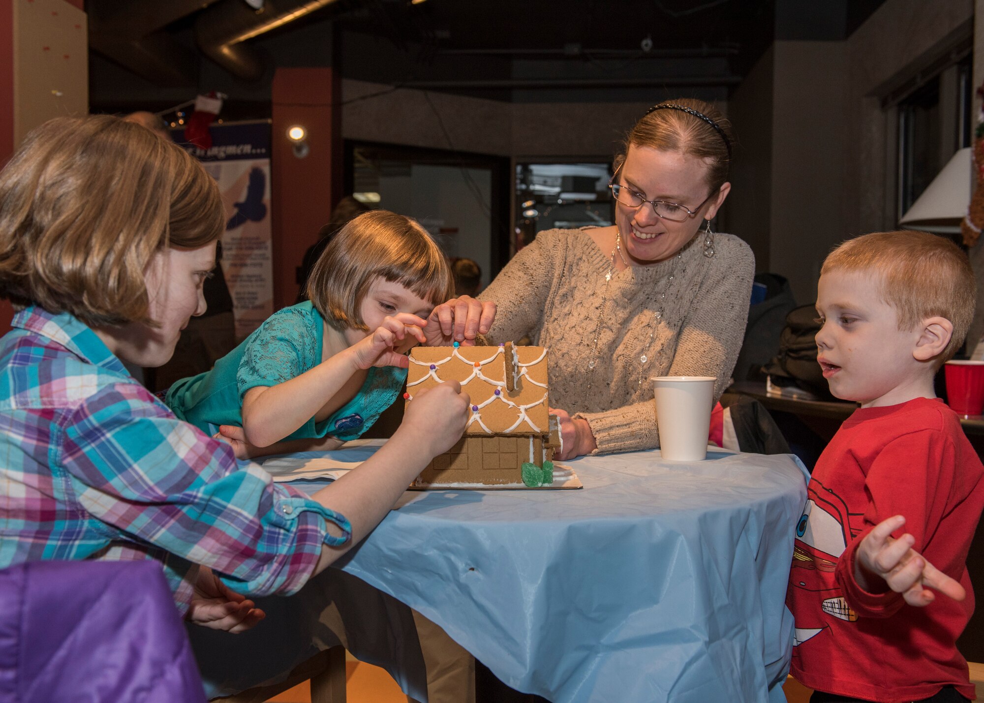 PETERSON AIR FORCE BASE, Colo. – Christy Lynch, wife of U.S. Air Force Academy Band member Airman 1st Class Warren Lynch, and their family decorate a gingerbread house Dec. 16, 2015 at the Eclipse Café. The Peterson Chapel provided all the supplies for Airmen and their families to have fun during the annual Gingerbread House Building Competition. (U.S. Air Force photo by Senior Airman Rose Gudex)