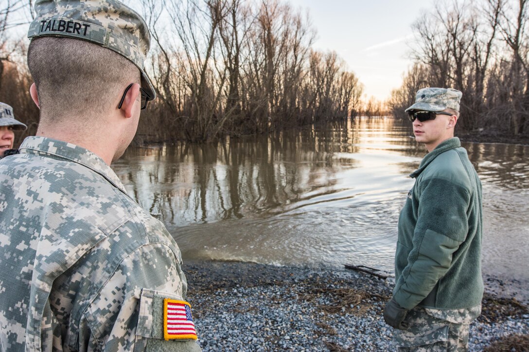 Missouri Guardsmen Spc. John Talbert, left, and Spc. Cole Schreiner observe a flooded roadway from a levee near East Prairie, Mo., Jan. 2, 2016.  Both are assigned to the 1140th Engineer Battalion, Missouri National Guard.  Missouri Air National Guard photo by Senior Airman Patrick P. Evenson