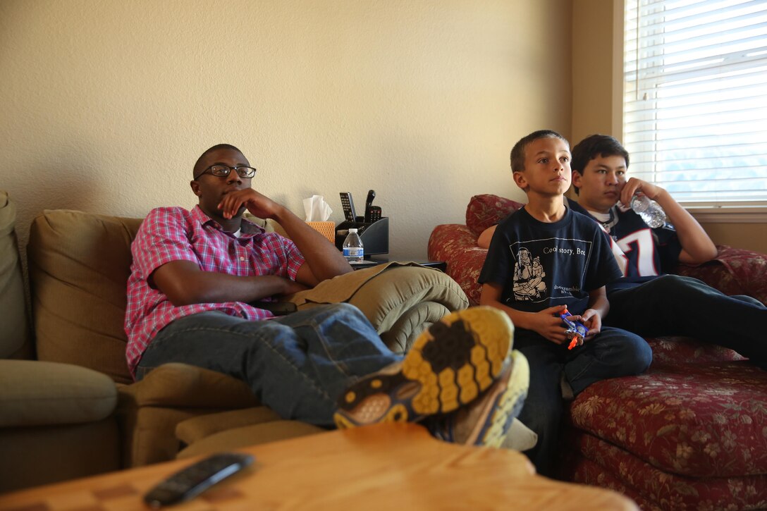 Cpl. Willie Williams, left, an administrative clerk with Marine Aircraft Logistics Squadron 11 and a Richmond, Virginia native, watches a basketball game with two children in a San Diego family’s home Dec. 25. Williams participated in the Great Escape’s “Home for the Holidays” program, which paired single Marines and Sailors to accommodating families during the holiday season. (U.S. Marine Corps photo by Sgt. Lillian Stephens/Released)