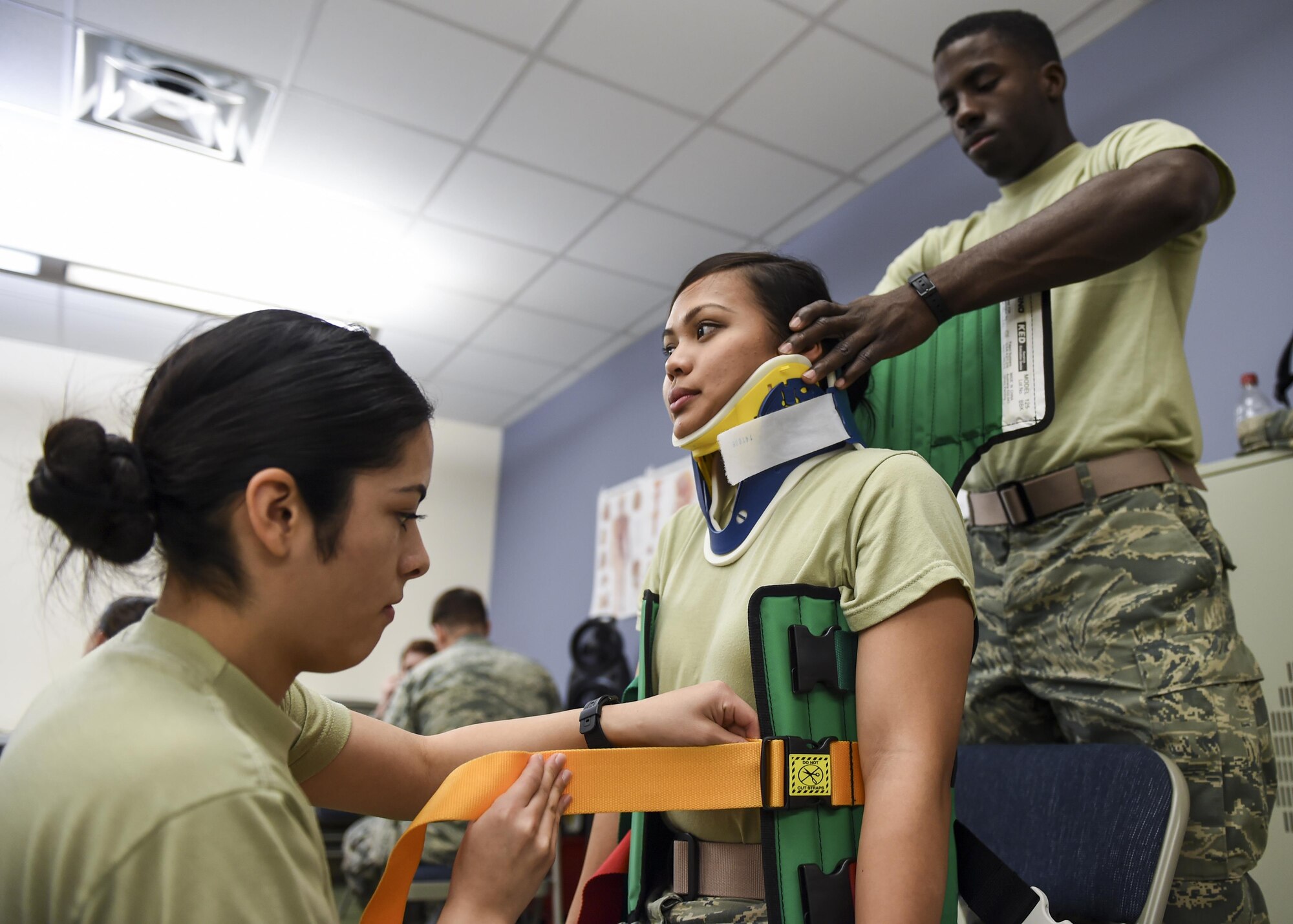 Airman Basic Ruby Del Real straps a Kendrick Extrication Device to Airman Basic Danielle Mortiz while Airman Carlos Todd braces her head for cervical spine precautions Dec. 17, 2015, at the Medical Education and Training Campus on Joint Base San Antonio-Fort Sam Houston, Texas. The Airmen are basic medical technician corpsman program students. The 59th Training Group develops, delivers and evaluates medical training for 75 medical treatment facilities and deployment operations worldwide
