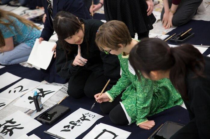 Mihiro Yamamoto, a member of the Calligraphy Club at Kannon High School, Hiroshima, Japan, teaches a home-schooler from Marine Corps Air Station Iwakuni how to write calligraphy during a calligraphy event at the Waki General Community Center, Waki Town, Jan. 4, 2016. Station residents and local residents only grow closer with each of these events.