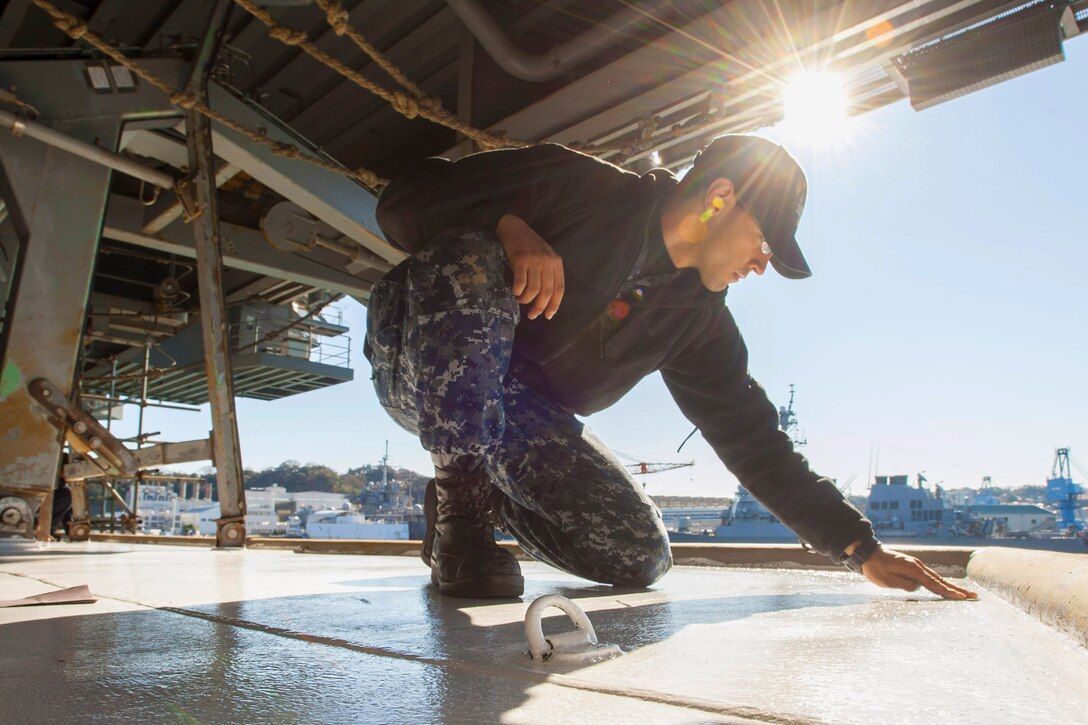 U.S. Navy Seaman Daniel Livas performs deck preservation checks on the port boat deck of the Navy's only forward-deployed aircraft carrier, the USS Ronald Reagan in Yokosuka, Japan, Jan. 1, 2016. The Ronald Reagan provides a combat-ready force that protects and defends the maritime interests of the United States, allies and partners in the Indo-Asia-Pacific region. U.S. Navy photo by Seaman MacAdam Kane Weissman