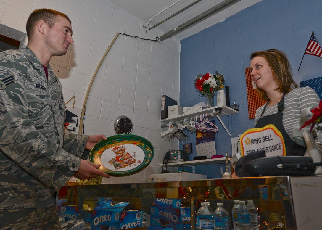 Senior Airman Brandon Gilbert, 28th Contracting Squadron specialist, left, hands a cookie platter to Magan Powell, B-One Thrift Store assistant manager, at Ellsworth Air Force Base, S.D., Dec. 18, 2015. The thrift store has three programs created to assist Airmen in need of household goods or clothing. For more information about the B-One Thrift Store and its programs, call (605) 385-5383 (U.S. Air Force photo by Airman Sadie Colbert/Released)