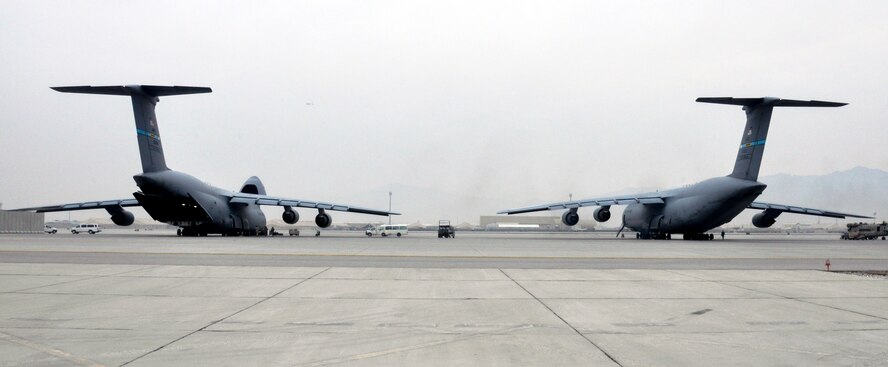 Two C-5M Super Galaxy aircrafts wait while crews from Task Force Destiny and 9th Airlift Squadron, Dover Air Force Base, Del., unload a helicopter at Bagram Air Field, Afghanistan, Dec. 26, 2015. The C-5M is the largest military transport aircraft in the world, capable of hauling 270,000 pounds of cargo. (U.S. Air Force photo by Tech. Sgt. Nicholas Rau)