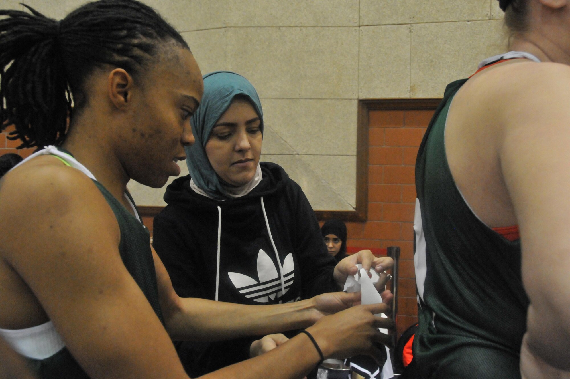 Kiara Nelson, 746th Expeditionary Airlift Squadron client system administrator, assists one of her teammates with jersey numbering, Jan. 2 at Al Gharafa Multi-Purpose Hall, Doha. Nelson assisted one of the Qatari women with taping numbers on the back of her teammates’ Jerseys to ensure the players were in regulations compliance with the tournament. (U.S. Air Force photo by Tech. Sgt. Terrica Y. Jones/released)