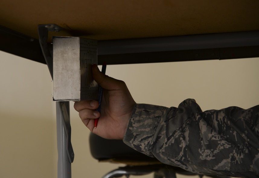 A 2nd Security Forces Squadron military working dog trainer places a training item under a table before conducting a detection exercise at Barksdale Air Force Base, La., Dec. 21, 2015. During detection training, instructors will hide various items in a pre-determined area for the handler and his dog to locate. (U.S. Air Force photo/Senior Airman Amanda Morris)