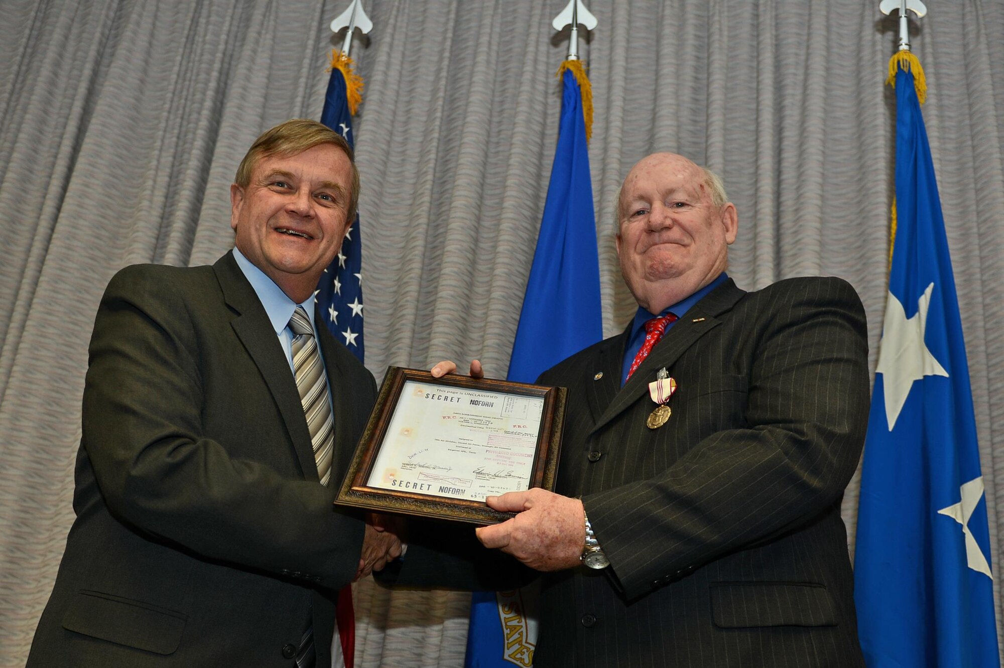 Dr. Charlie O'Connell, Air Force history office representative, presents Herb Mason, Air Force Special Operations Command historian, a memento during his retirement ceremony on Hurlburt Field, Fla., Jan. 7, 2016. The frame holds the title page to the first history document that then Airman 3rd Class Herb Mason wrote in his career. (U.S. Air Force Staff Sgt. Melanie Holochwost) 