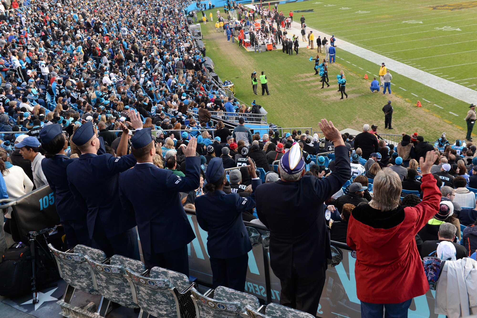 Seven military service members wave to the crowd, Jan. 3, 2016, at Bank of America Stadium in Charlotte, North Carolina. The National Football League highlighted four Seymour Johnson Air Force Base Airmen as well as a retired veteran with his wife, keeping one chair open to pay tribute to POW/MIAs in the stadium’s USO of North Carolina Row of Honor. (U.S. Air Force photo/Airman 1st Class Ashley Williamson)
