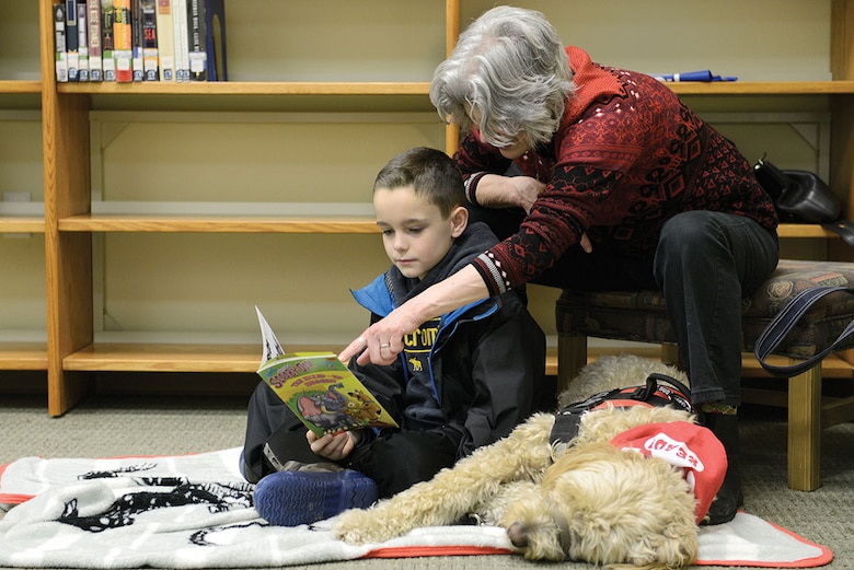 Braden Blair, 8, reads to Swivelshot, a goldendoodle therapy dog, and Sheila Barrett, dog handler, at the Paws to Read program at the Joint Base Elmendorf-Richardson Library, Dec. 19, 2015. The JBER Library and Midnight Sun Service Dogs work together to make this program possible. Braden is the son of Master Sgt. Daniel Blair, 673d Civil Engineer Squadron firefighter. (U.S. Air Force photo by Airman Valerie Monroy)