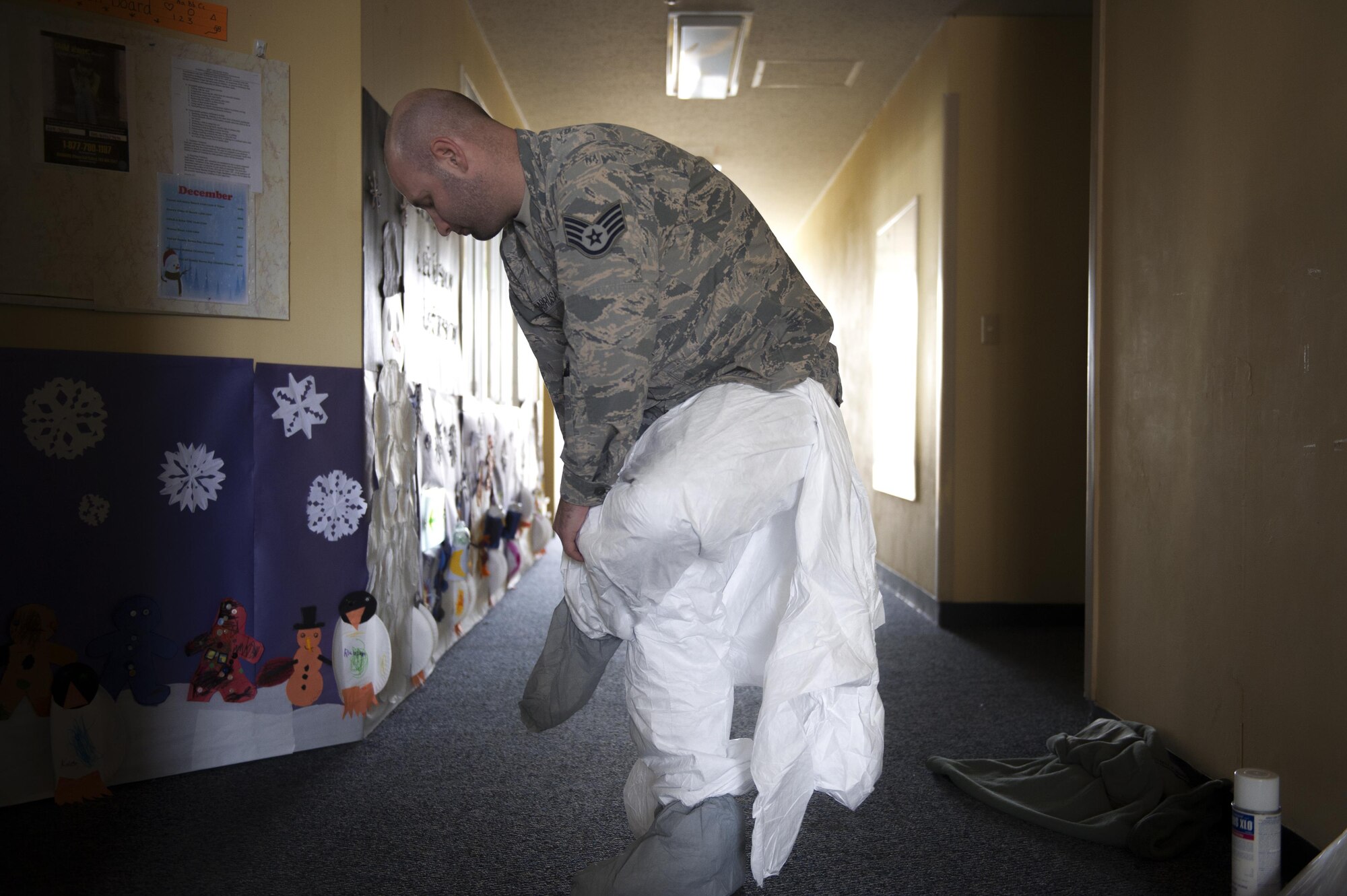 Staff Sgt. Brandon Cenarrusa, 374th Civil Engineer Squadron pest management craftsman, dons a protective suit before entering the crawlspace of the Child Development Center at Yokota Air Base, Japan, Jan. 6, 2016. 374 CES utilize preventative and immediate response maintenance practices to ensure that facilities remain pest free. (U.S. Air Force photo by Airman 1st Class Delano Scott/Released)