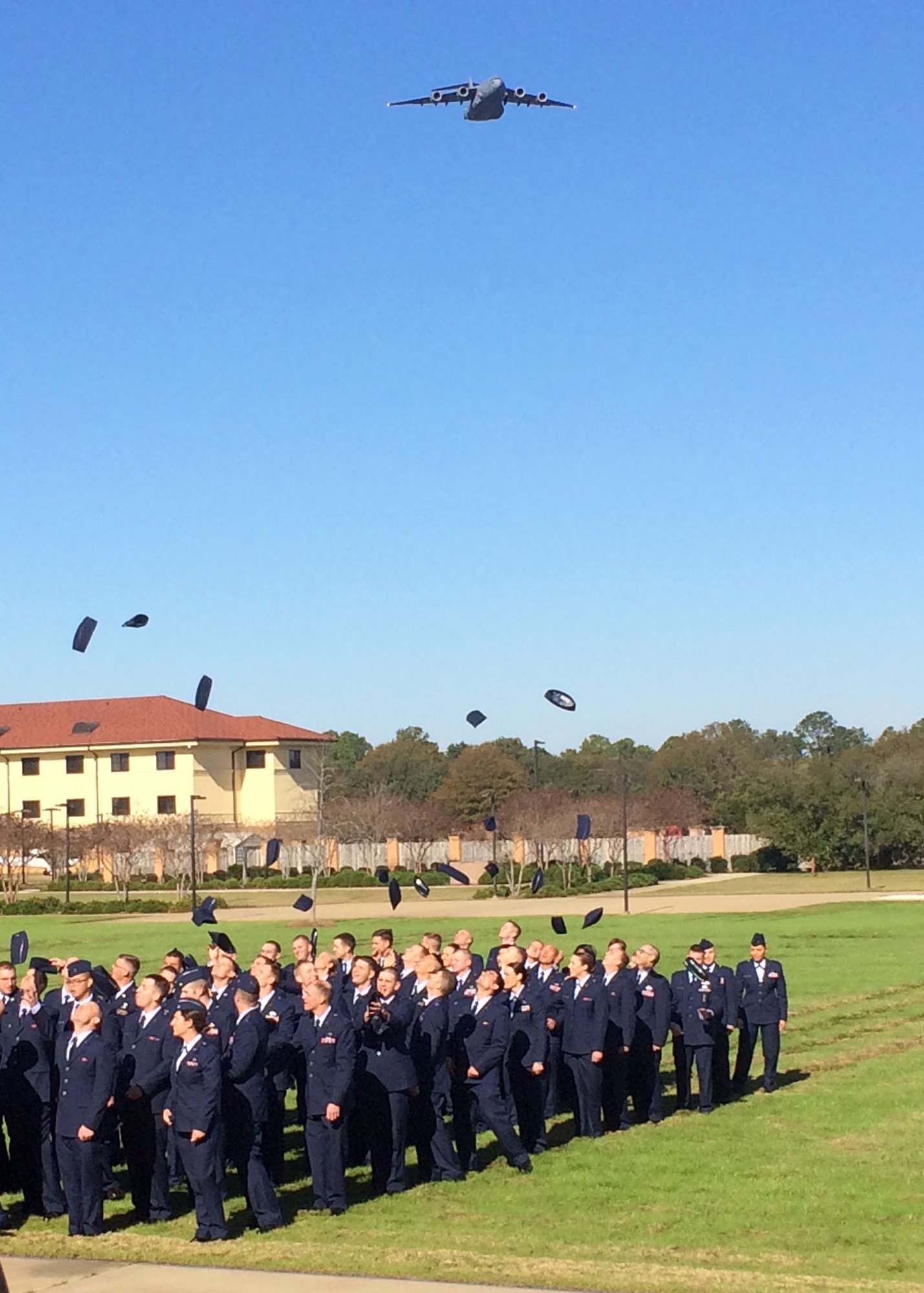 A C-17 Globemaster III flies overhead as newly commissioned 120th Airlift Wing 2nd Lieutenants Matthew Hall, Alissa Engel, Bradford Lewis, and Joshua Briggs join fellow classmates in throwing their hats into the air in celebration of their graduation from Officer Training School at Maxwell Air Force Base, Ala. Dec. 18, 2015. (U.S. Air National Guard photo by Capt. Kenneth Fechter/Released)