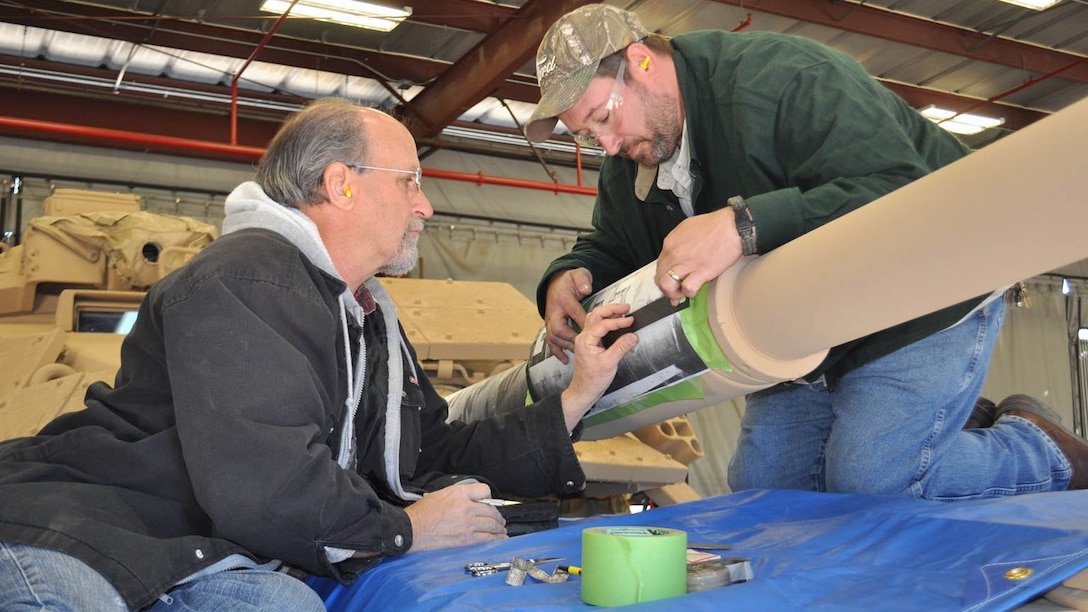 Marine Depot Maintenance Command artisans stencil the gun barrel of the Genesis II, an M60A1 Main Battle Tank, as part of the final steps in a restoration project between MDMC and National Museum of the Marine Corps, Dec. 15, 2015.