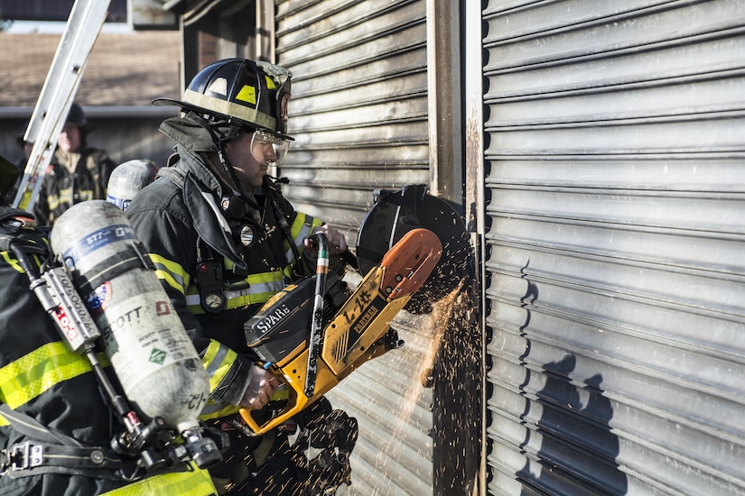 A New York City firefighter works to cut the lock off a rollup door with a circular saws on the front of a burning building during a live-fire exercise at the New York City Fire Academy on Russell Island in New York City, Jan. 6, 2016. Drill sergeant leaders from the United States Army Drill Sergeant Academy on Fort Jackson, S.C., were at the Fire Academy Jan. 4-8, to observe training as part of a collaboration between the Fire Department of New York and the Center for Initial Military Training providing lessons learned and offering alternate training methods for new recruits. (U.S. Army photo by Sgt. 1st Class Brian Hamilton)