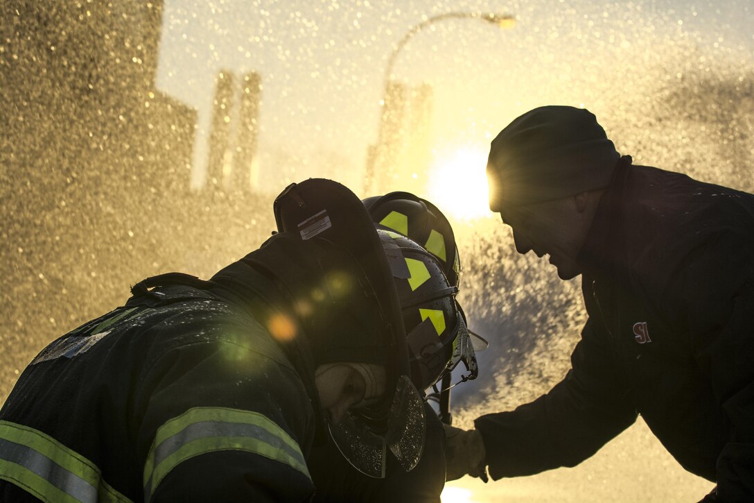 Capt. Matthew Cregin, an Instructor with the New York City Fire Academy, assists probationary firefighters in their second week of training at the school on Russell Island in New York City, Jan. 6, 2015. The new firefighters are performing a drill known as motivation alley in which pairs of two firefighters must travel 100 feet down a road from a kneeling position carrying a charged 1¾-inch fire hose to put out a mock flame. Drill sergeant leaders from the United States Army Drill Sergeant Academy on Fort Jackson, S.C., were at the Fire Academy Jan. 4-8, to observe training as part of a collaboration between the Fire Department of New York and the Center for Initial Military Training providing lessons learned and offering alternate training methods for new recruits. (U.S. Army photo by Sgt. 1st Class Brian Hamilton)