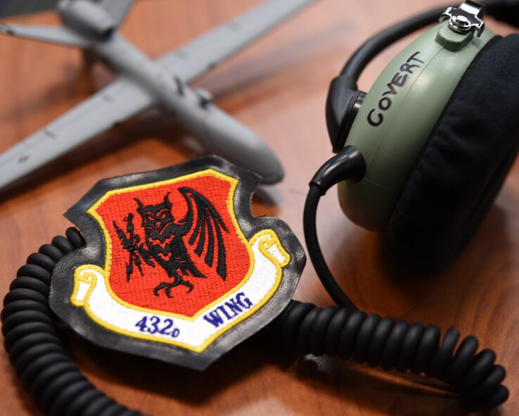 Airmen from the 432nd Wing/ 432nd Expeditionary Wing at Creech Air Force Base, Nevada participate in Career Day at the Boys and Girls Club Jan. 7, 2016 in Las Vegas, Nevada. The wing patch on the left displays an owl holding two lightning bolts, and symbolizes global strike capability. The headset on the right is a piece of equipment used by pilots and sensor operators of remotely piloted aircraft. In the background is a small model MQ-9 Reaper, an aircraft piloted at Creech. (U.S. Air Force photo by Airman 1st Class Kristan Campbell/released).