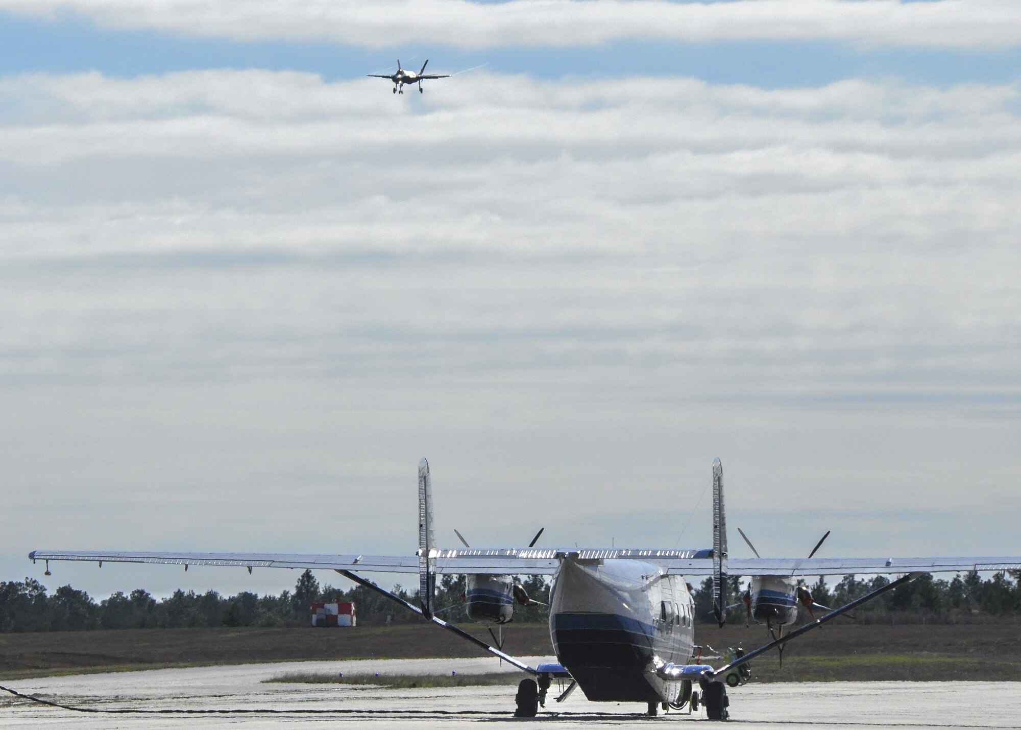 An F-35 Lightning II performs a fly by to the runway as a C-145 Skytruck waits for its next mission Jan. 5 at Duke Field, Fla.  (U.S. Air Force photo/Dan Neely)