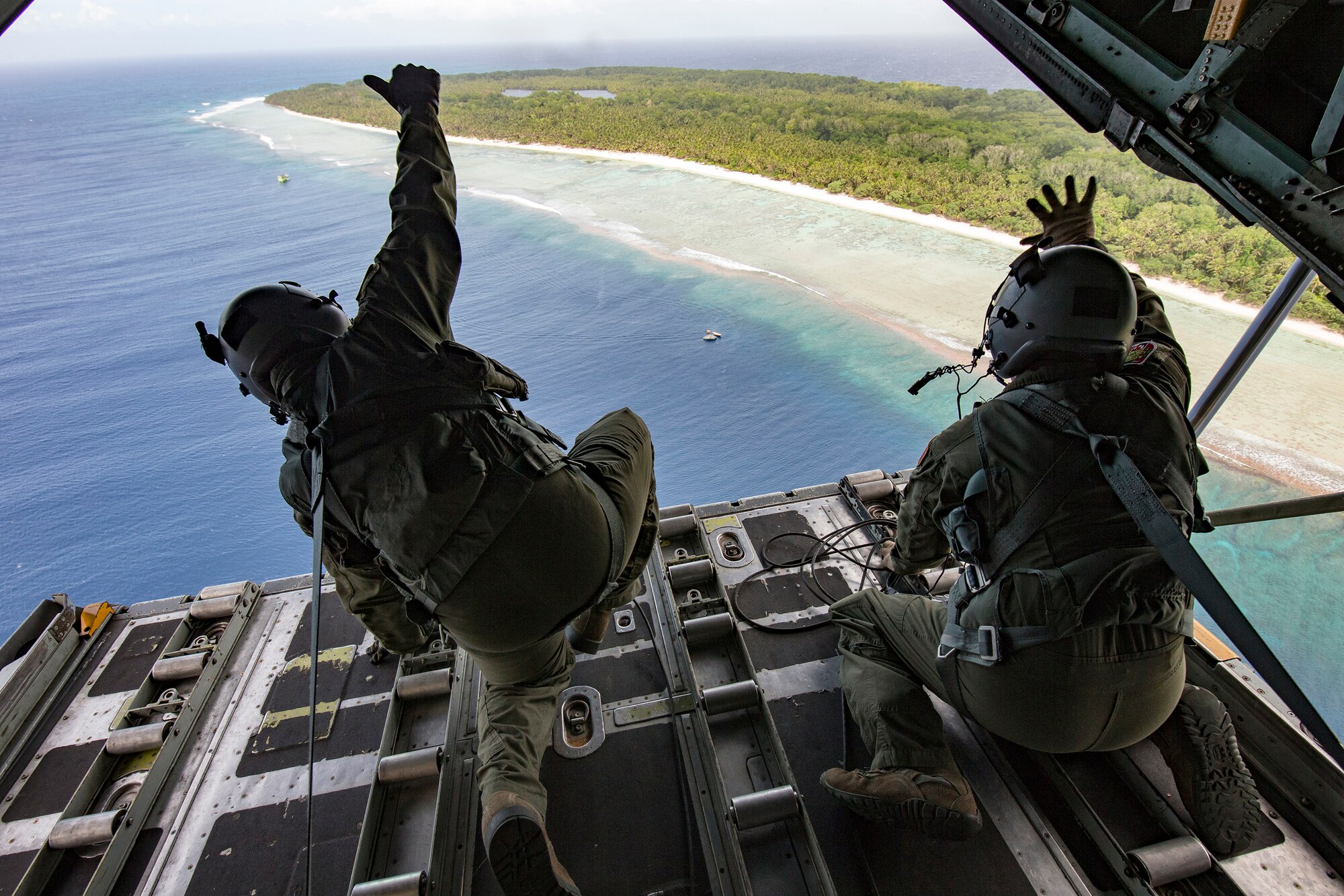 Loadmasters from 36th Airlift Squadron wave out the back of a C-130H Hercules to the people of Pulusuk , Federated States of Micronesia Dec. 13, 2015, during Operation Christmas Drop. Every December, C-130H Hercules aircrews from Yokota head to Andersen Air Force Base to execute low-cost, low-altitude humanitarian airdrops to islanders throughout the Commonwealth of the Northern Marianas, Federated States of Micronesia, Republic of Palau. These islands are some of the most remote locations on the globe spanning a distance nearly as broad as the continental U.S. It is the longest-running Department of Defense humanitarian airdrop operation with 2015 being the first trilateral execution with support from Japan Air Self-Defense Force and Royal Australian Air Force. (U.S. Air Force photo by Osakabe Yasuo/Released)
