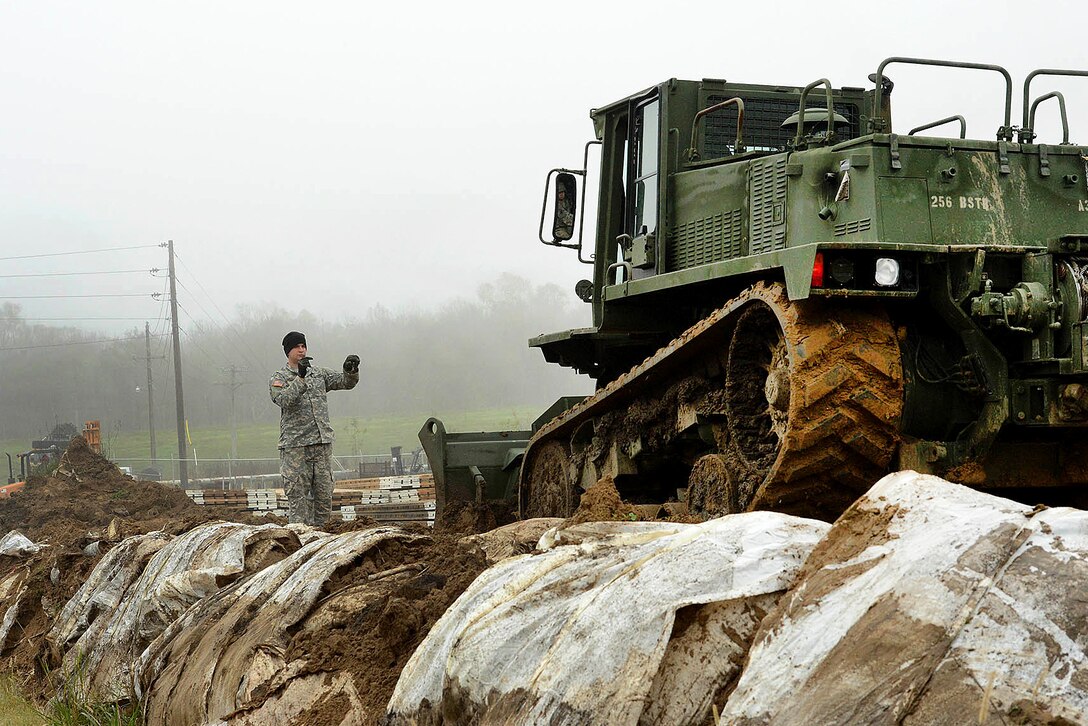 Army Pvt. Taner Mansur, operating a M105 deployable universal combat earthmover, receives directions from another soldier while repairing a levee in advance of expected river flooding in Krotz Springs, La., Jan. 8, 2016. Mansur is assigned to the Louisiana National Guard’s 769th Brigade Engineer Battalion, 256th Infantry Brigade Combat Team. Louisiana Air National Guard photo by MSgt. Toby Valadie