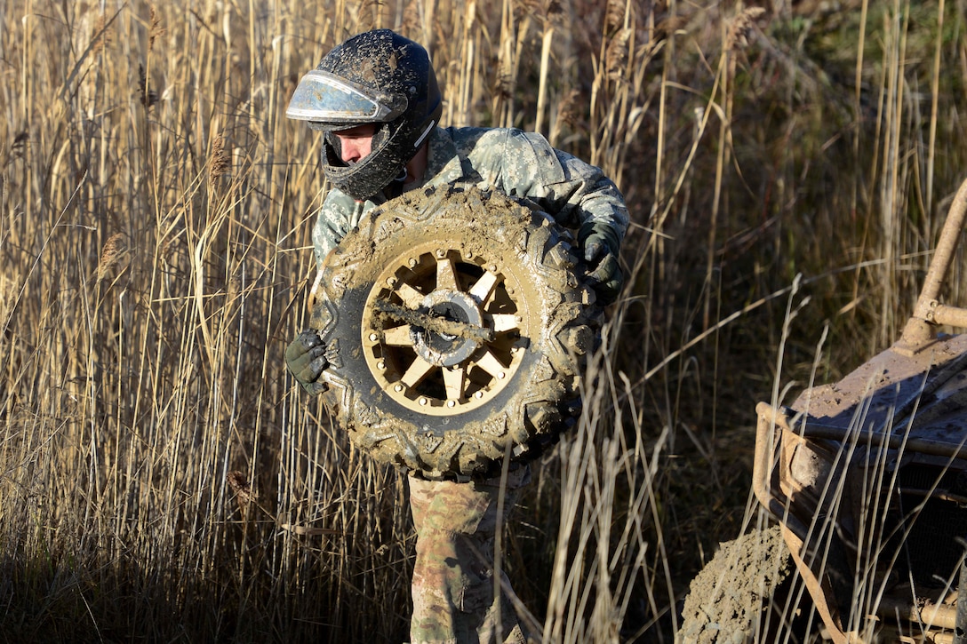 A U.S. Soldier carries a tire to change out another while testing the capabilities of the MRZR4 LT-All Terrain Vehicle in the Boeblingen Local Training Area, Germany, Jan. 5, 2016. U.S. Army photo by Jason Johnston