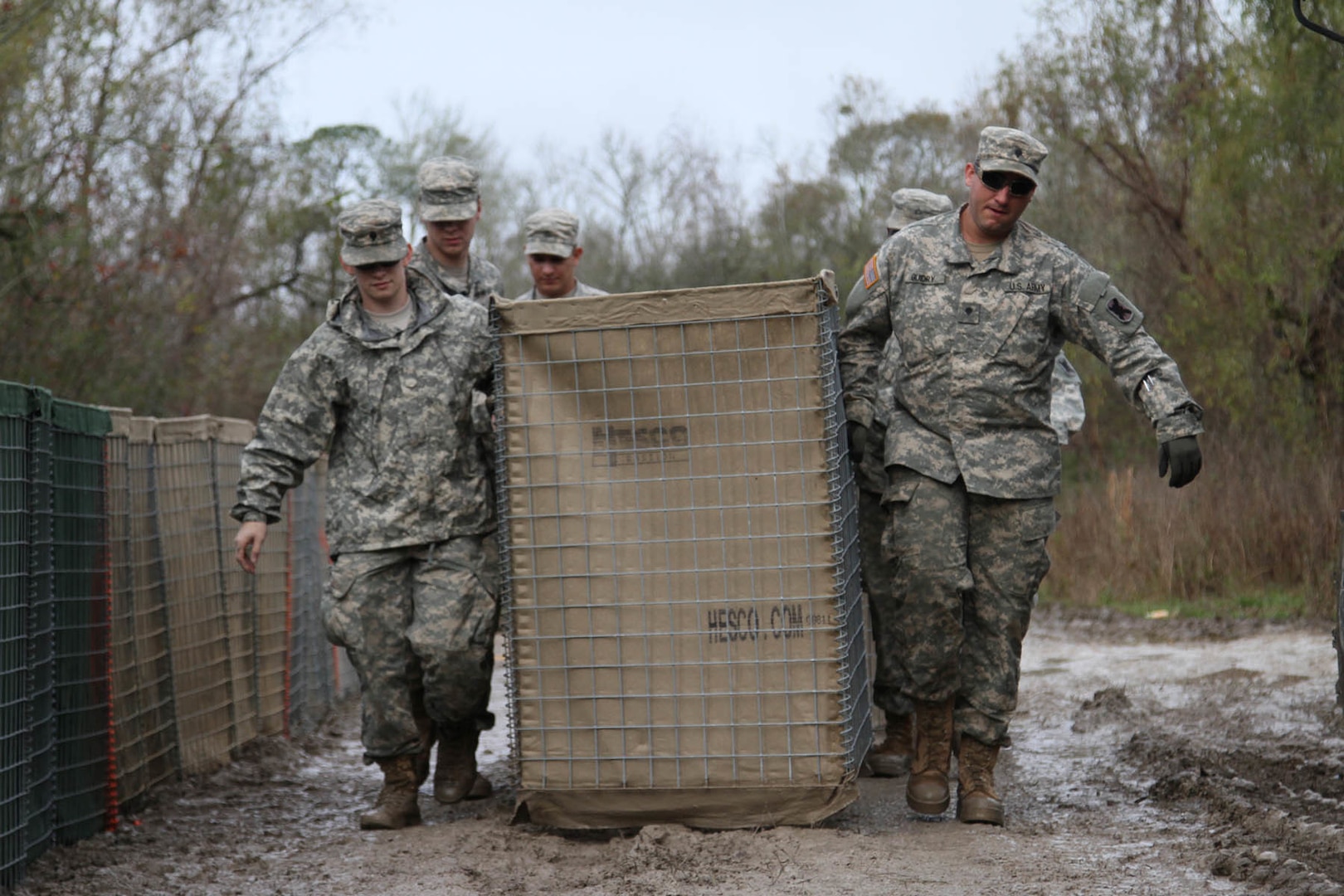 Louisiana National Guard Spc. Scott Mouton, of Baton Rouge, Spc. Mason Guidry, of Breaux Bridge, and other Guard members carry a HESCO barrier on Avoca Island near Morgan City, La., Jan. 9, 2016. The barrier will be used in the construction of a 2-mile long levee to prevent backwater flooding from reaching Morgan City and other towns in South Louisiana due to high river levels. 