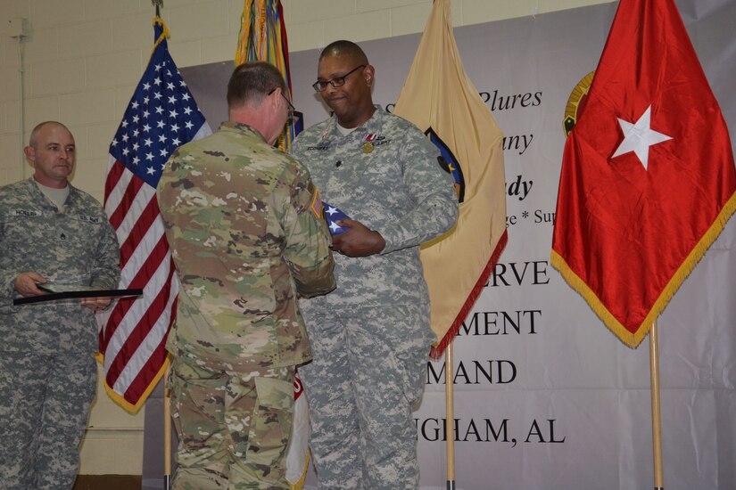 Brig. Gen. Jeffrey Doll presents Lt. Col. Alan Sconiers with a retirement flag during his retirement ceremony. Sconiers’ career spanned over 29 years of military service in the Army National Guard and Army Reserve.  He received the Meritorious Service Medal along with several certificates of appreciation and a memento of an eagle made out of Alabama clay from the Army Reserve Sustainment Command (also pictured is Staff Sgt. William Hollis, awards bearer).   