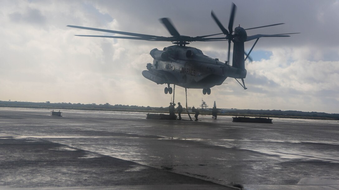 A CH-53E from Marine Heavy Helicopter Squadron 465 hovers above as Marines with Combat Logistic Battalion 11 rush in to attach 6,200-pound weight to the helicopter aboard Marine Corps Air Station Miramar, Calif., Jan. 7. Marines with CLB-11 support HMH-465 during daytime external lift training to prepare for future deployments. 