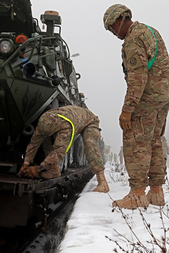 U.S. Army Sgt. Ryan Powell, right, supervises Spc. Tyler Minnick, left, as Minnick removes a chock block from a Stryker armored fighting vehicle during railhead operations in Konotop, Poland, Jan. 11, 2016. Before vehicles can be moved from the train, soldiers must conduct cold-start procedures and remove equipment used to hold the vehicles in place during transit. Both soldiers are infantryman assigned to Knight Troop, 3rd Squadron, 2nd Cavalry Regiment. U.S. Army photo by Sgt. Paige Behringer