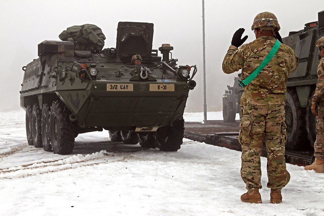 U.S. Army Sgt. 1st Class Richard Rodriguez, right, uses hand and arm signals to guide a Stryker armored fighting vehicle during railhead operations in Konotop, Poland, Jan. 11, 2016. U.S. Army photo by Sgt. Paige Behringer
