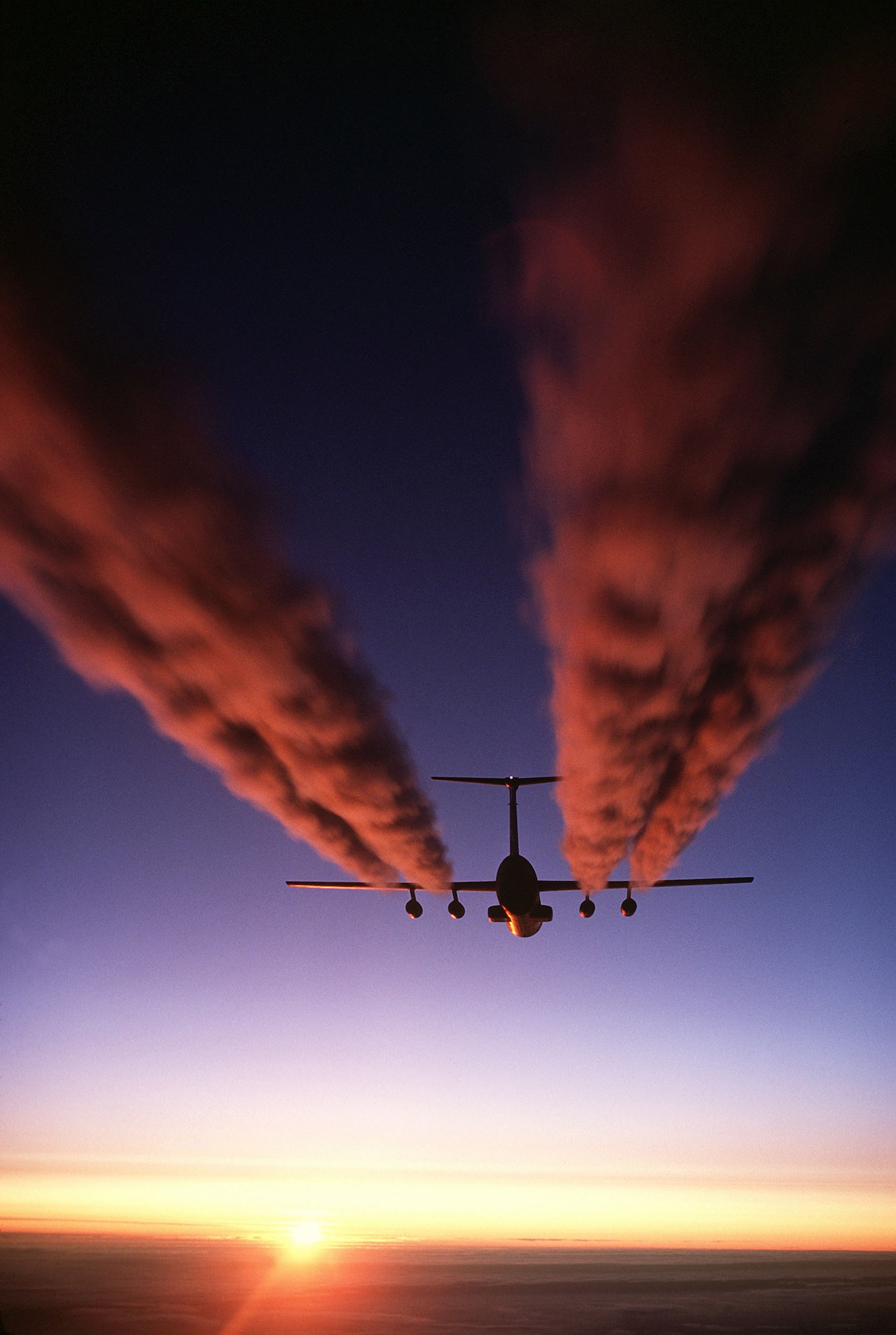 A C-141B Starlifter aircraft leaves four plumes of exhaust behind it as it prepares for an airdrop. (U.S. Air Force file photo) 