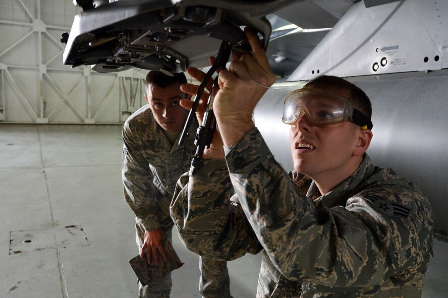 A U.S. Air Force weapons load crew member evaluates Senior Airman Jackson Crammer, 20th Aircraft Maintenance Squadron, 77th Aircraft Maintenance Unit weapons load crew member, on Crammer and his team’s ability to prepare and successfully load munitions onto an F-16CM Fighting Falcon during a weapons load crew of the quarter competition at Shaw Air Force Base, S.C., Jan. 8, 2016. Evaluators assessed the accuracy, safety, and time it took for them to load munitions onto the aircraft. (U.S. Air Force photo by Senior Airman Diana M. Cossaboom)