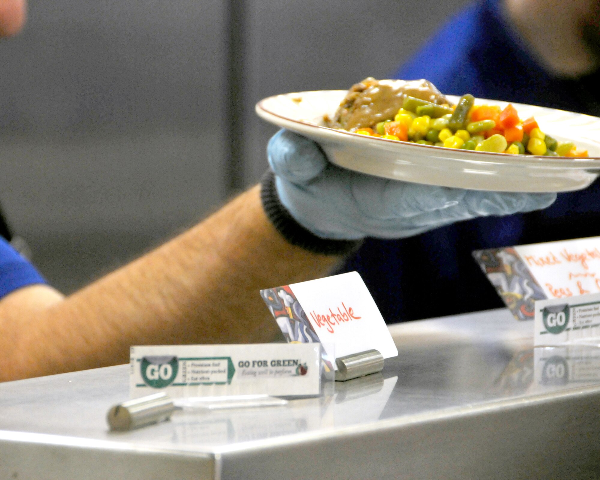 A dining facility worker hands a plate of “green” foods to an Airman during the 120th Airlift Wing’s regularly scheduled drill Nov. 8, 2015. Small labels stating the “color” for each food item are displayed on the serving line making it easy for Airmen to choose healthier meals. (U.S. Air National Guard photo by Tech. Sgt. Michael Touchette/Released)
