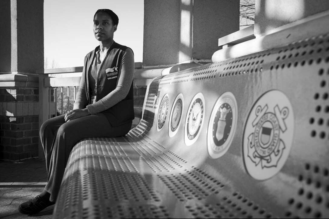 Senior Master Sgt. Jennifer O'Quinn, Veterans Affairs volunteer and 11th Wing Equal Opportunity director, sit outside Loch Raven VA Community Living and Rehabilitation Center in Baltimore, Md., Dec. 8, 2015. The bench presents all five U.S. military branches logos and represents a resting place for the men and women the VA cares for at Loch Raven. (U.S. Air Force photo by Airman 1st Class Philip Bryant/Released)