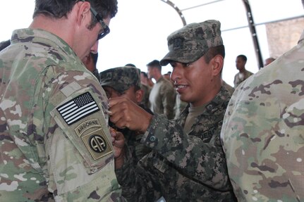 A Honduran soldier with the 2nd Honduran Airborne Brigade exchanges pins with a U.S. Service member with the Special Operations Command South (Forward) 7310 after a static-line training exercise involving both nations on Soto Cano Air Base, Honduras, January 11, 2016. Exercises such as these provide an opportunity to exchange knowledge and enhance partner nation interoperability. (U.S. Army photo by Maria Pinel)