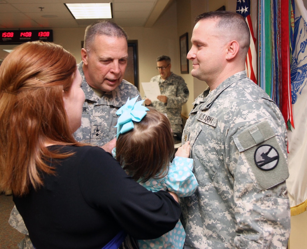 U.S. Army Reserve Maj. Gen. Scottie D. Carpenter, commanding general, 84th Training Command, Fort Knox, Ky., watches as Maj. James A. Watson's daughter, Emmary, who is held by his wife, Christie, pins major rank on him during his promotion ceremony during the Command Headquarters and Headquarters Detachment's Battle Assembly at the Command's headquarters on Fort Knox, Jan. 9, 2016. (U.S. Army Photo by Sgt. 1st Class Clinton Wood/Released).