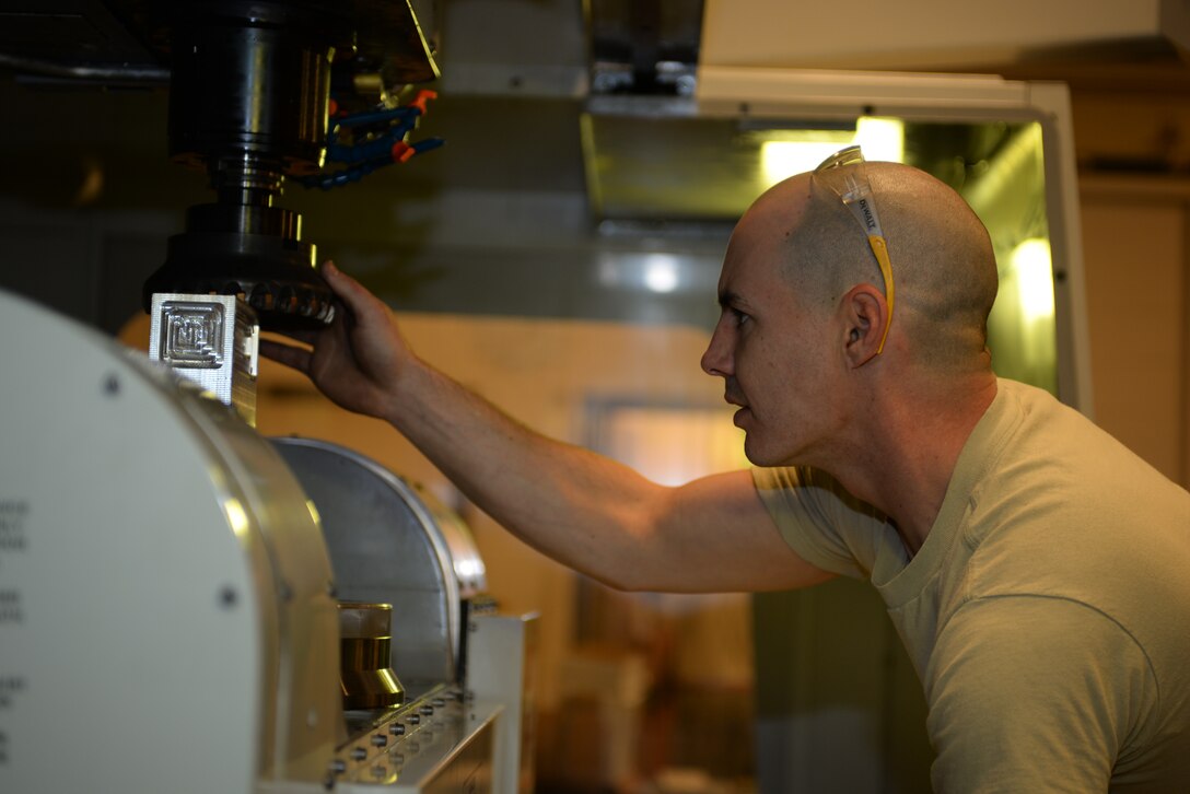 Staff Sgt. Adam Hebert, 28th Maintenance Squadron production supervisor, inspects a Haas VF 6 machine before cutting a metal block at Ellsworth Air Force Base, S.D., Jan. 6, 2016. The machine receives coding from a 3D model computer program and then uses that to cut out specific measurements and create a desired piece. The metals flight creates aircraft parts that cannot be ordered through a supplies list. (U.S. Air Force photo by Airman Sadie Colbert/Released)