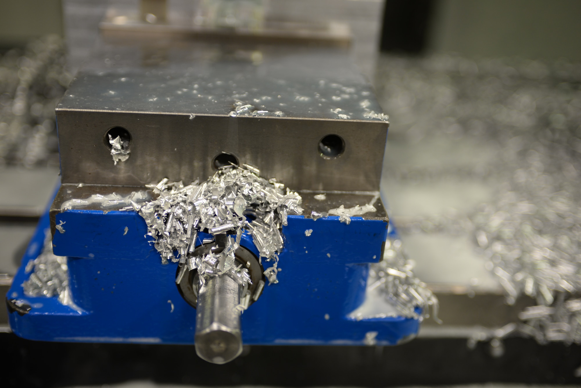 Chips from a metal block sit on a computer numerical control base at Ellsworth Air Force Base, S.D., Jan. 6, 2016. The 28th Maintenance Squadron metals flight creates parts like pulleys and over-wing fairing brackets; discarding excess materials like the chips into a bin for safety control. The flight creates aircraft parts that cannot be ordered through a supplies list. (U.S. Air Force photo by Airman Sadie Colbert/Released)