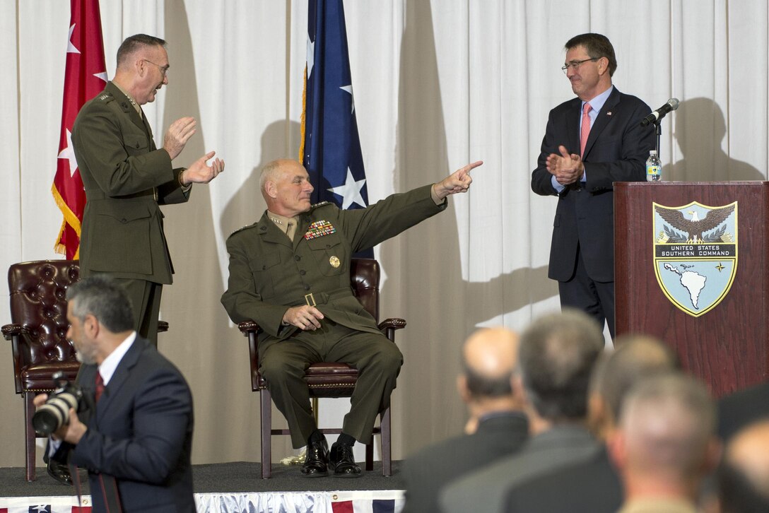 Marine Corps Gen. John F. Kelly, seated, reacts to a standing ovation from Defense Secretary Ash Carter, right, and Marine Corps Gen. Joseph F. Dunford Jr., chairman of the Joint Chiefs of Staff, during the change-of-command ceremony at the command's headquarters in Miami, Jan. 14, 2016. DoD photo by EJ Hersom