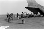 Medical personnel use litters to transport Cpl. Richard Ramirez, 1st Marine Division, and other wounded to a C-141B Starlifter aircraft.  The patients are being medically evacuated from Al-Jubayl Air Base to Germany for treatment of wounds received during Operation Desert Storm.