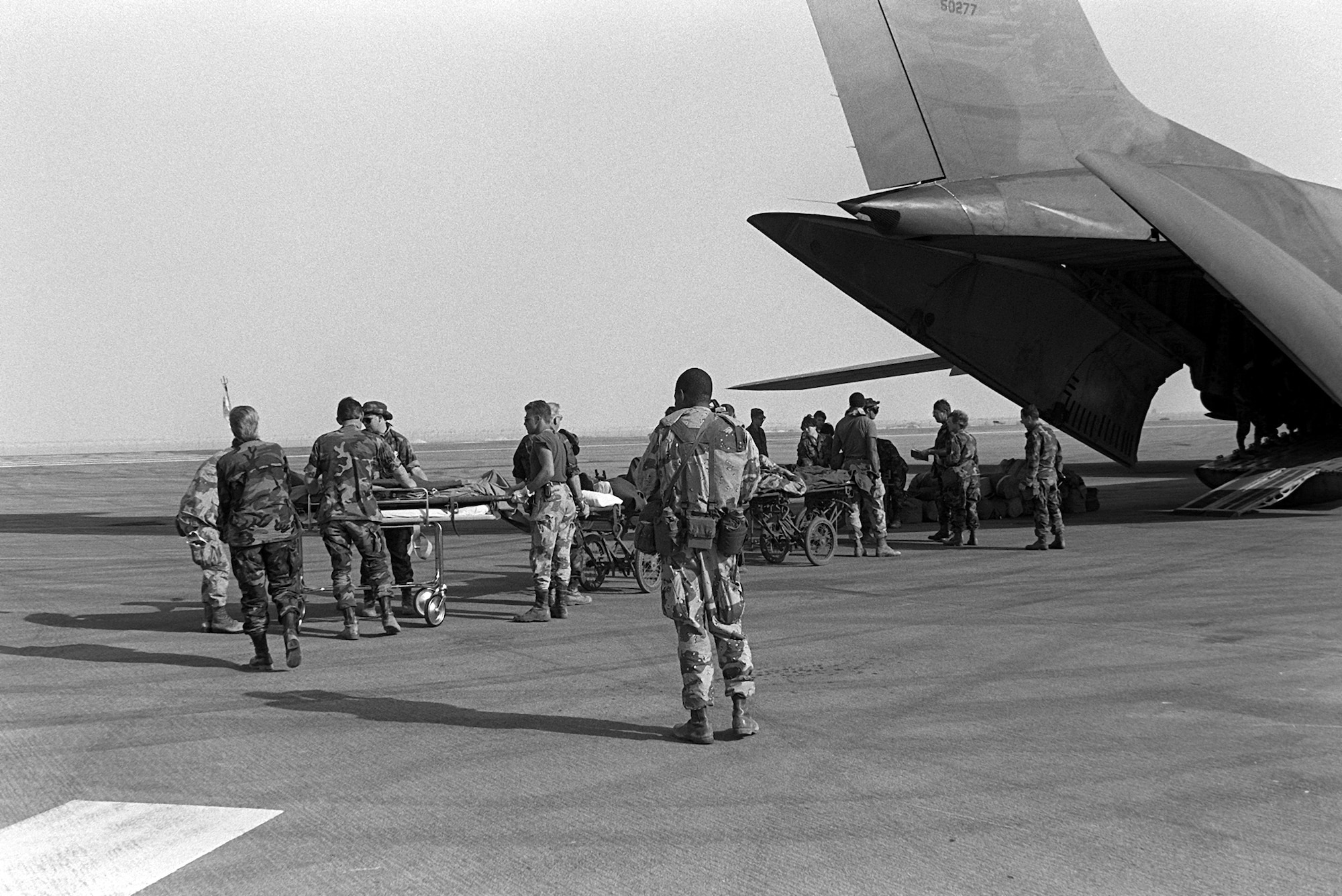 Medical personnel use litters to transport Cpl. Richard Ramirez, 1st Marine Division, and other wounded to a C-141B Starlifter aircraft. The patients are being medically evacuated from Al-Jubayl Air Base to Germany for treatment of wounds received during Operation Desert Storm.