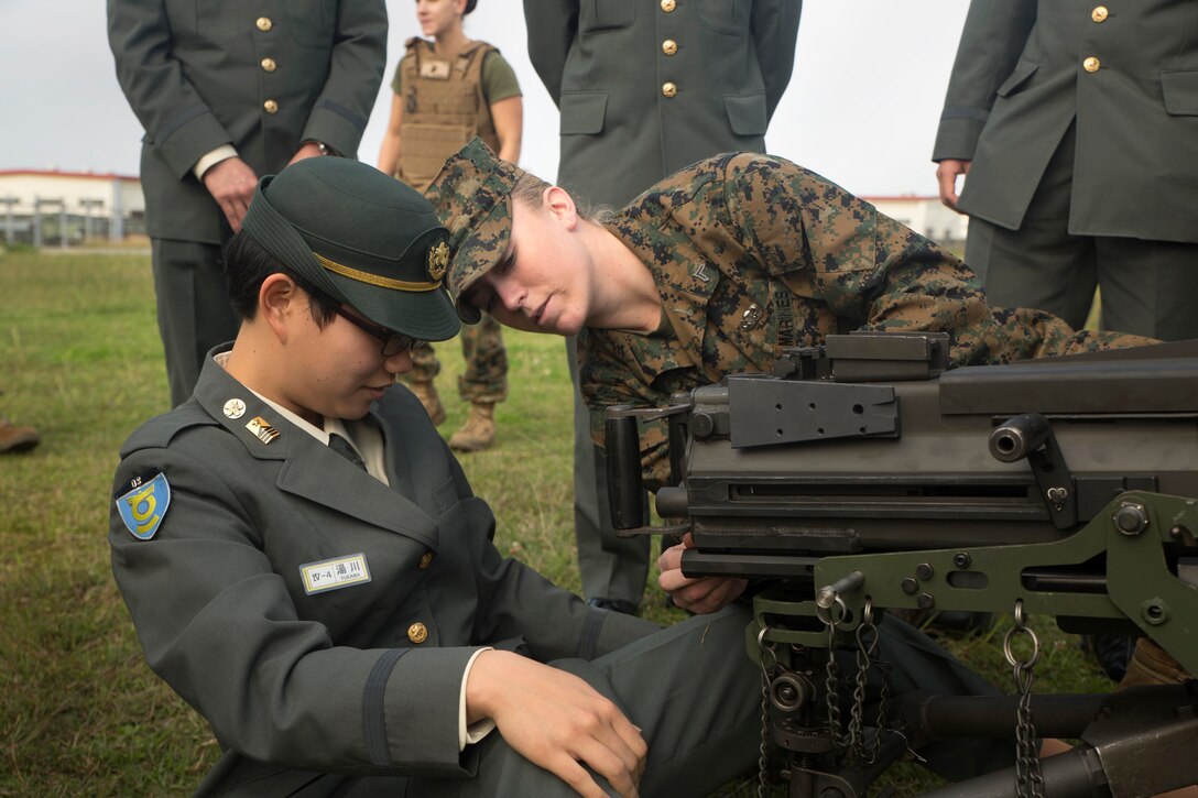 Cpl. Malynn Ochsner shows Japan Ground Self-Defense Force officer candidate Ayako Yukawa how to operate a MK19 machine gun, MOD 3 on Camp Kinser, Okinawa, Japan, Jan. 15. Three hundred and sixty JGSDF officer candidates visited Combat Logistics Regiment 35 to complete joint and combined operation requirements. The cadets watched Marine Corps Martial Art Program demonstrations, learned the capabilities of various machine guns the Marine Corps uses, and observed a static display of motor transportation vehicles. Ochsner, from Pflugerville, Texas, is a distribution management specialist with 3rd Supply Battalion, CLR-35, 3rd Marine Logistics Group, III Marine Expeditionary Force. (U.S. Marine Corps photo by Cpl. Robert Williams Jr./Released)