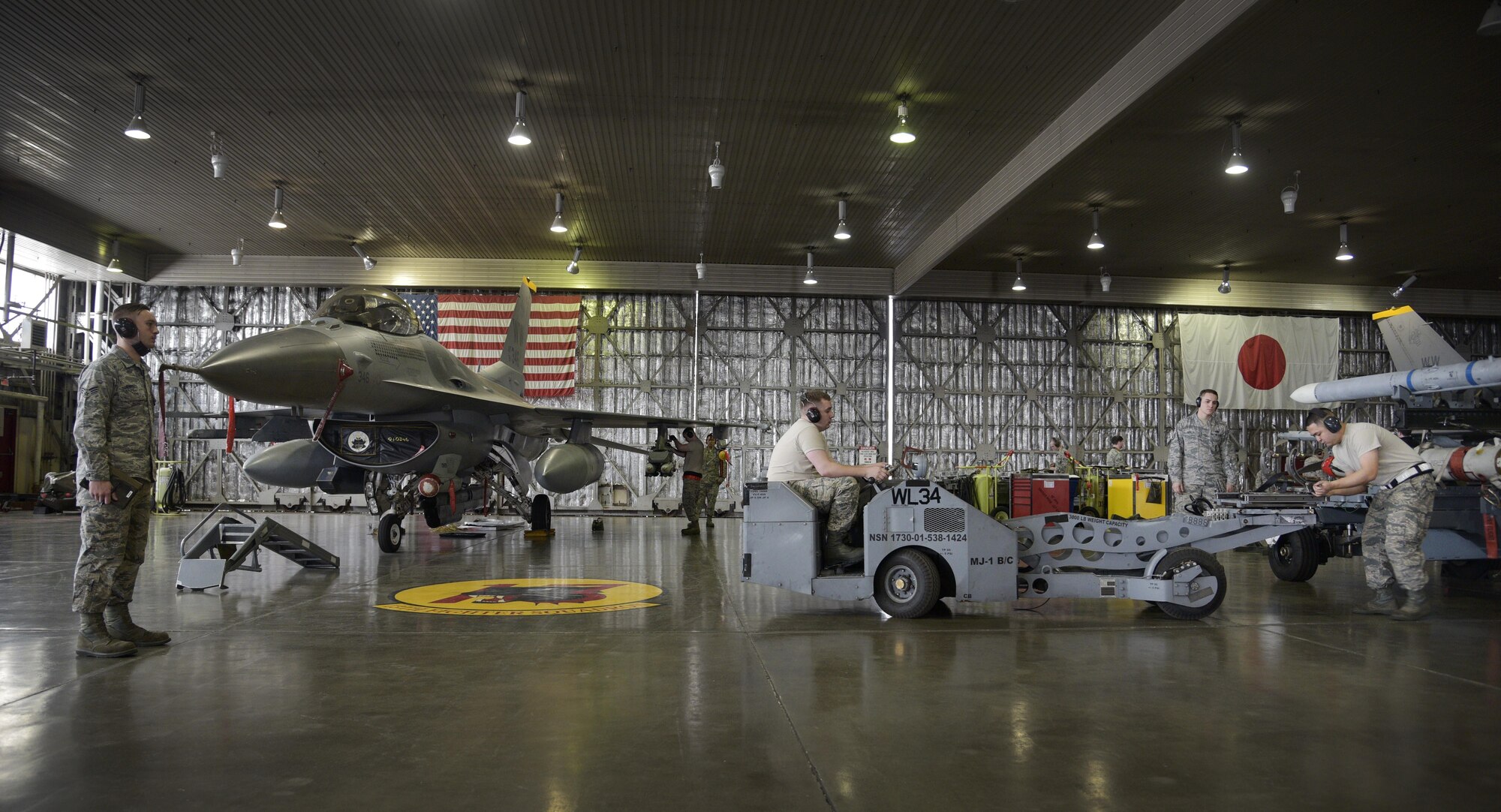 A weapons load team from the 35th Aircraft Maintenance Squadron prepares to load a weapons system while being inspected by a standardization load crew from the 35th Maintenance Group during a quarterly weapons loading competition at Misawa Air Base, Japan, Dec. 30, 2015. The objective of the weapons load crew competition was to gauge how quickly and efficiently teams of Airmen are able to arm an F-16 Fighting Falcon. (U.S. Air Force photo/Senior Airman Deana Heitzman)